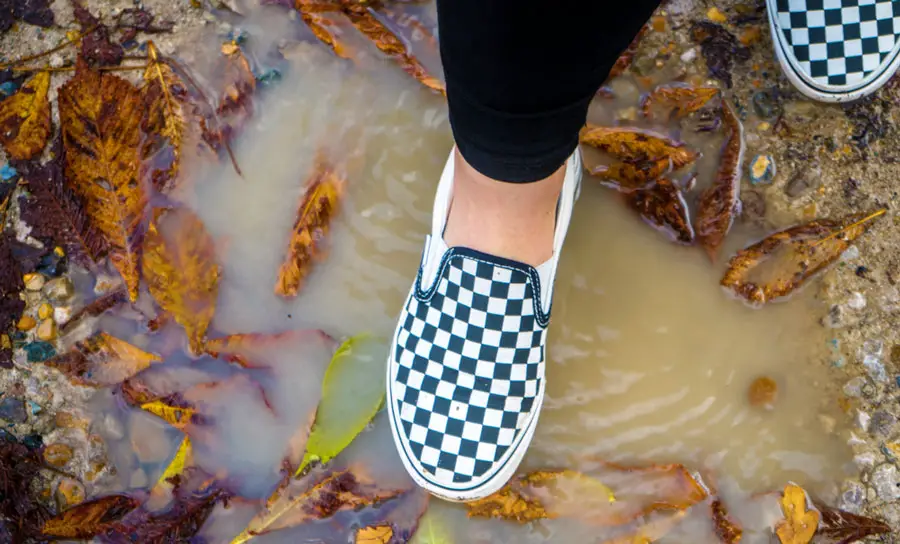 A woman wearing a Vans Checkerboard Slip-on steeping in puddle